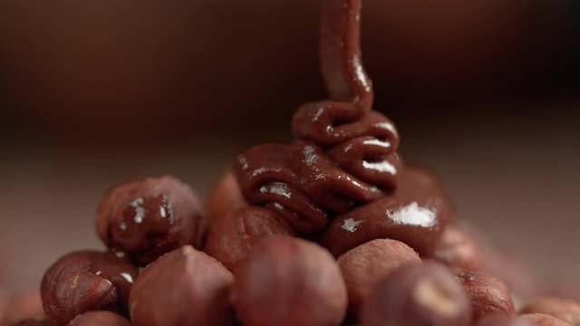 SLOW MOTION, MACRO, DOF: Tasty homemade chocolate hazelnut spread is poured over raw unpeeled hazelnuts. Yummy nougat butter flows over a heap of organic brown hazelnuts. Gourmet sweet cocoa spread.