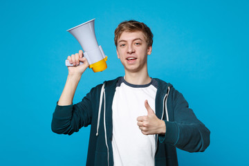 Portrait of attractive young man in casual clothes showing thumb up holding megaphone isolated on...