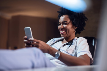 Happy African American nurse text messaging on mobile phone.