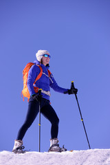 randonneuse en raquette dans la neige sur un beau ciel bleu et un sac orange fluo puis des lunettes de soleil