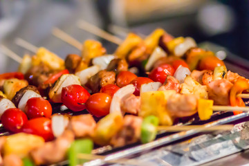 Seafood and beef barbecue (BBQ) skewered on bamboo sticks with pie apple, tomato, onion and chili are grilling on the stove for barbecue party. Barbecue skewers meat kebabs with vegetables at night.