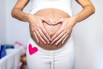 Close up of Pregnant Woman Making a Heart with her Hands on her Stomach.