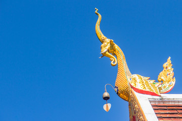 Fototapeta na wymiar Beautiful golden naga sculptures on the church roof under the blue sky background at Wat Phra That Doi Tung, one of which is believed to contain the left collarbone of Lord Buddha.
