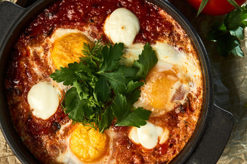 Traditional shakshuka with eggs, tomatoes and parsley in a frying pan
