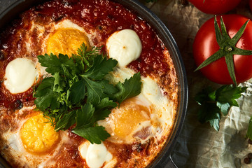 Traditional shakshuka with eggs, tomatoes and parsley in a frying pan