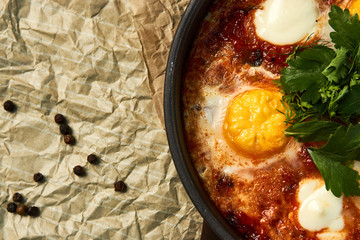 Hot shakshuka with eggs, tomatoes and parsley in a frying pan, close-up