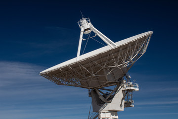 Very Large Array side view of white radio antenna satellite dish against a deep blue sky, horizontal aspect