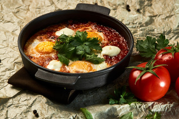 Hot shakshuka with eggs, tomatoes and parsley in a frying pan, close-up