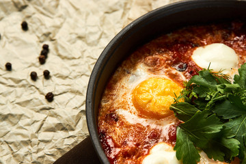 Hot shakshuka with eggs, tomatoes and parsley in a frying pan, close-up
