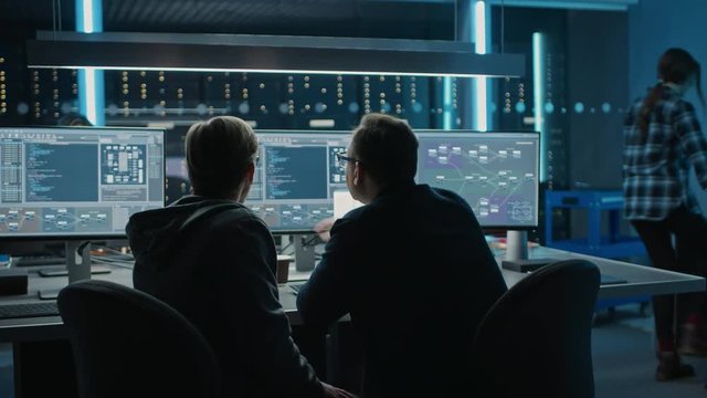 Two Professional IT Programers Discussing Blockchain Data Network Architecture Design and Development Shown on Desktop Computer Display. Working Data Center Technical Department with Server Racks 