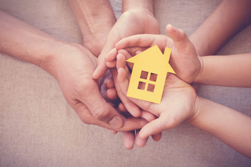 Adult and child hands holding yellow house,  home protection, foster care, family home and homeless...