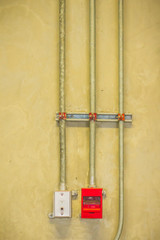 Red fire alarm pull box emergency and fire fighters telephone with conduit pipeline on concrete wall.