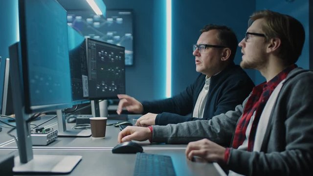 Two Professional IT Programers Discussing Blockchain Data Network Architecture Design and Development Shown on Desktop Computer Display. Working Data Center Technical Department with Server Racks 