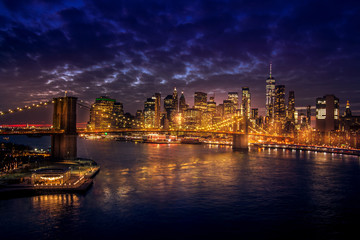 Fototapeta na wymiar Must see when visiting New York City. View of Lower Manhattan and Brooklyn at sunset. Night scene. Light trails. City lights. Urban living, travel, real estate and transportation concept