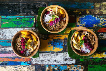 Close up four smoothie bowls made with mango, banana, granola, grated coconut, dragon fruit, chia seeds and mint on colored background