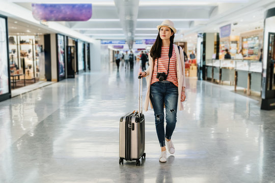 full length of elegant confident travel young girl shopping tax free area. beautiful lady with luggage suitcase walk in duty free store shop while waiting for plane departure in lobby gate terminal