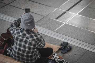Homeless man sitting on the street in the shadow of the building. He begging for  help and money....