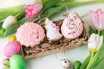 Colorful Easter cookies with frosting icing decor, painted colorful eggs and tulips on light table. Springtime holiday concept, greeting background with copy space, traditional food
