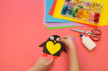 Penguin made of paper on a pink background. Workshop. Children's hands glue crafts.