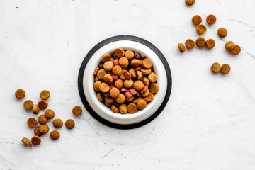 Dry dog food in bowl on white stone backgorund top view space for text