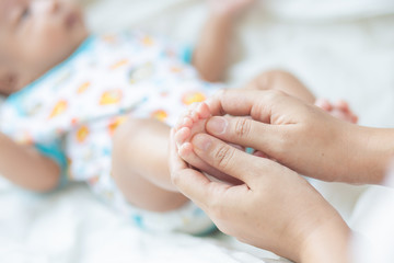 Baby boy foot massage by mom on white blanket
