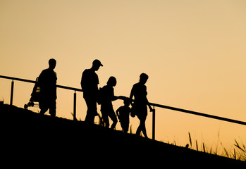 Silhouette image of lovely Caucasian family  walking down the hill during going for recreation activity in twilight evening of summer.