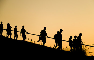 Fototapeta na wymiar Silhouette image of Asian and Caucasian tourists walking down the hill in twilight evening. 