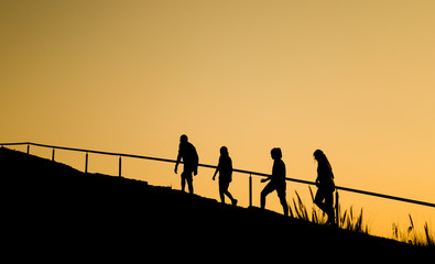 Silhouette image of lovely Caucasian family of four people walking in line up the hill in twilight evening for recreation and relaxation in weekend day. 