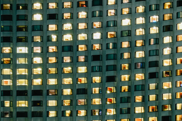Fototapeta na wymiar Frontal view of the night facade of building with a lot of windows and Lamp in many room within hotel.