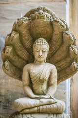 Beautiful Buddha statue made of sand stone and cover with Naga heads. Stone Buddha statue with seven Phaya Naga heads. Outdoor stone seated Buddha image protected by 7 heads Naga spreads cover on top.