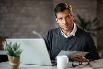 Businessman analyzing reports and working on a computer in the office.