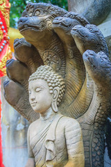 Beautiful Buddha statue made of sand stone and cover with Naga heads. Stone Buddha statue with seven Phaya Naga heads. Outdoor stone seated Buddha image protected by 7 heads Naga spreads cover on top.