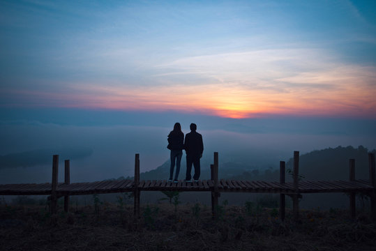 View on hill lover couple silhouette standing on a wooden bridge