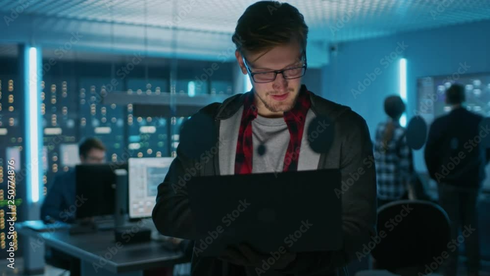 Poster portrait of a smart focused young man wearing glasses holds laptop. in the background technical depa