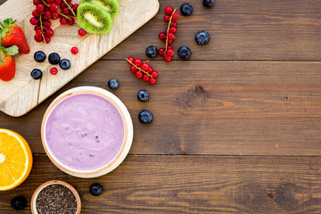 Cook trendy breakfast. Acai smoothie bowl near cutting board with fresh fruits, berries, chia seeds on dark wooden background top view copy space