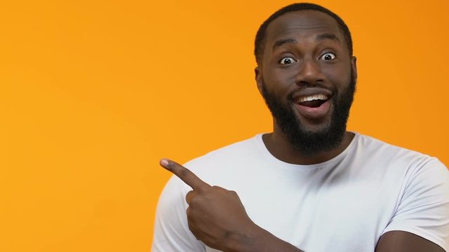 Excited black male pointing at bright background, place for your text, surprise