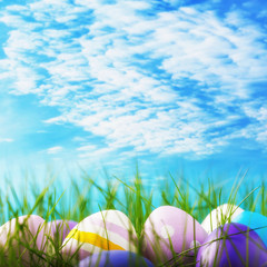 Easter eggs decorated in various colors in the grass against the sky with copy space