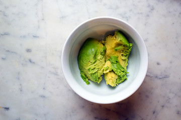 Avocado in white bowl with white marble chopping board