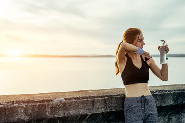 Asian woman is workout and running at the morning, she is warm up her body and drinking  fresh water. Healty and sport lifestyle concept.