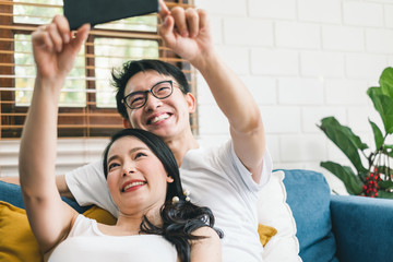 Obraz premium Young Asian couple lover taking selfie by mobile phone at home, relax and lifestyle at home concept