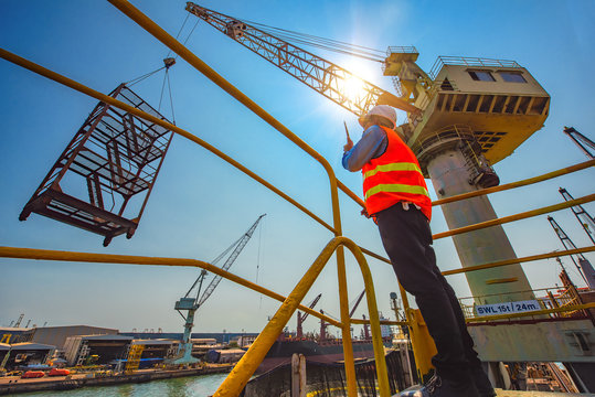 stevedore or foreman, engineering, loading master talks to crane driver by walkie talkie for safety lifting  the goods or shipment, lifting by gantry crane, working at risk on the high level insurance