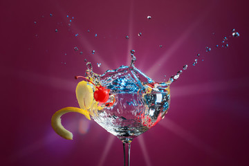 Colorful cocktail in glass with splashes garnished with lemon and cherries.