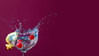 Colorful cocktail in glass with splashes garnished with lemon and cherries.