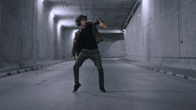 Serious Cool Young Hipster Man with Long Hair is Energetically Dancing Hip Hop in a Lit Concrete Tunnel