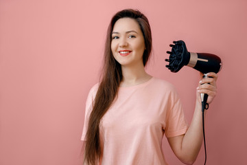 young smiling woman with  hairdryer in hands on pink background