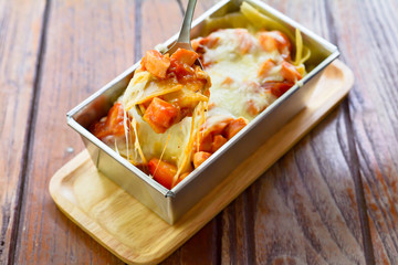 Delicious sausage lasagna and cheese on metal spoon for eat in lunch. Served on wooden table.
