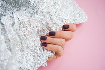 Young woman's hand with beautiful manicure on pink background holding metallic shiny paper.
