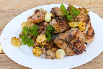 Grilled pork meat with onion and parsley on wooden table
