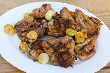 Grilled pork meat with onion and parsley on wooden table