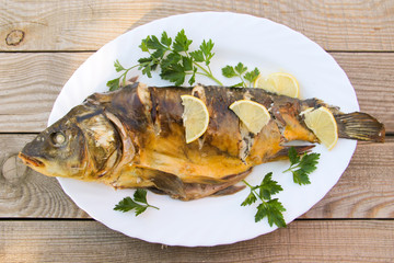 Tasty baked carp in white plate on wooden table. Top view